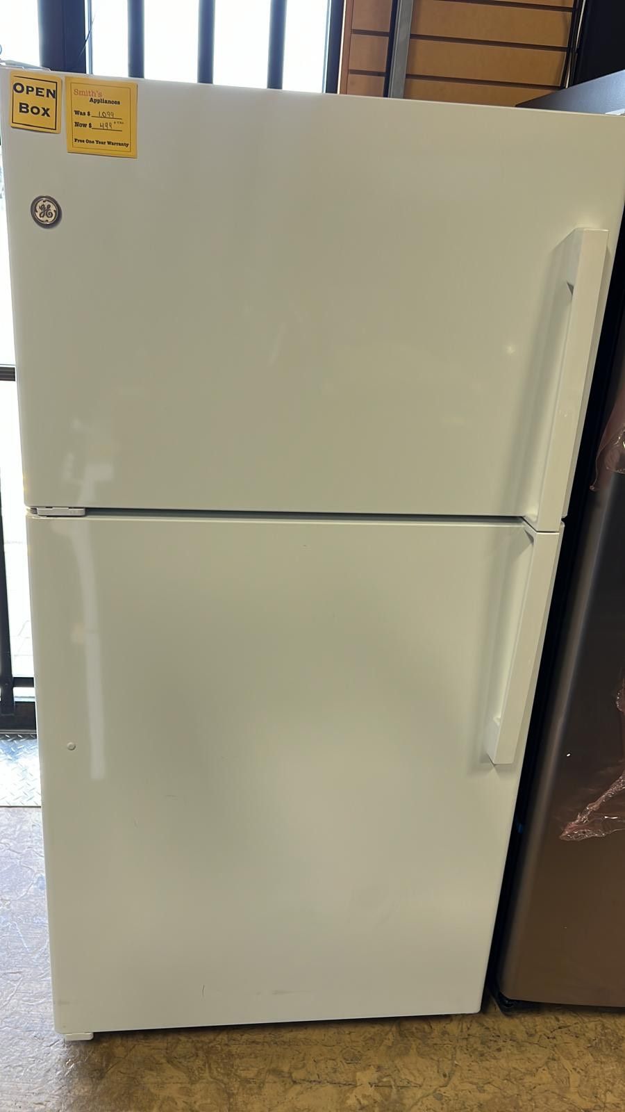 A white refrigerator with a yellow sticker on it is sitting on a wooden floor.
