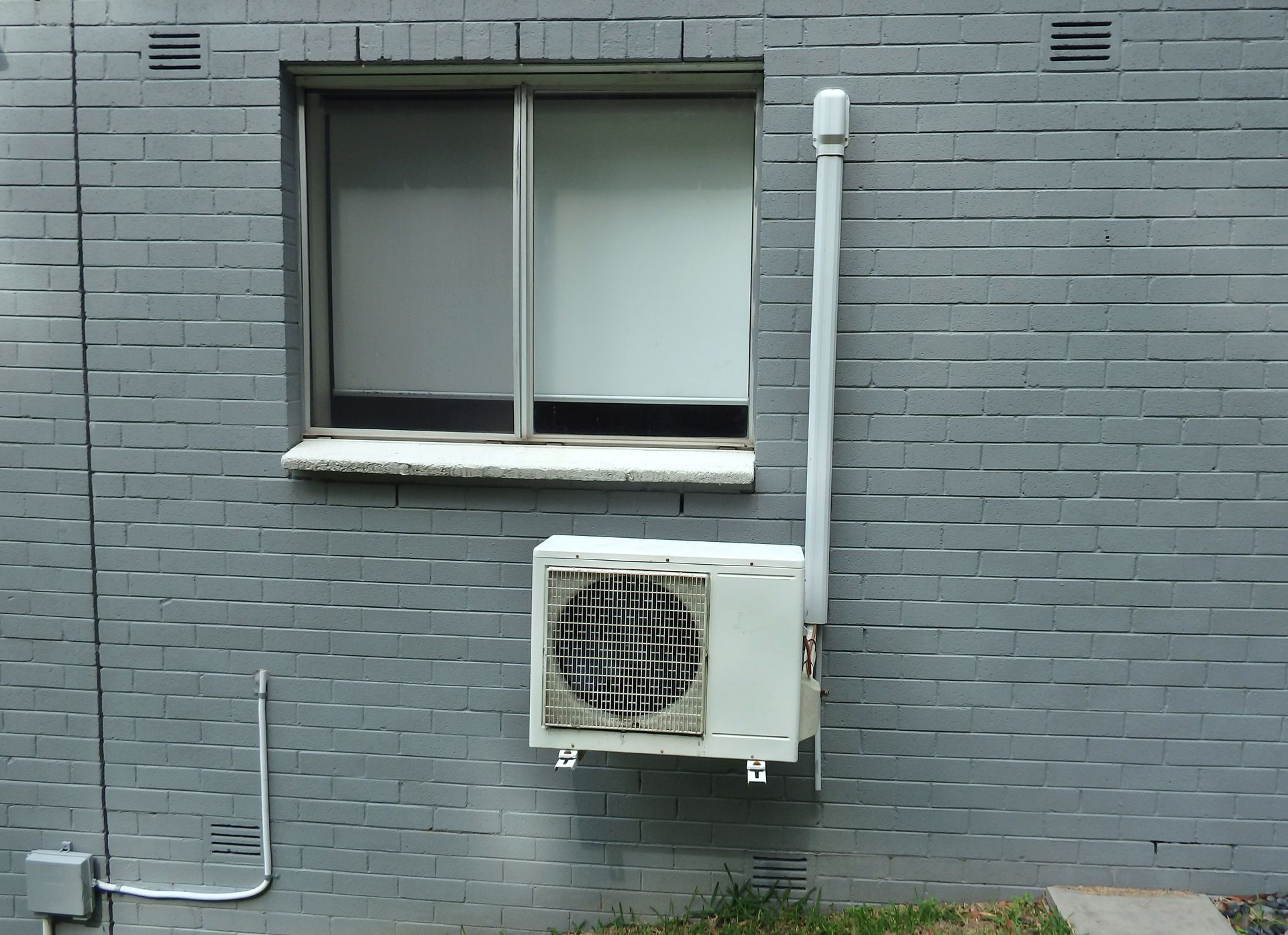 Gray brick building exterior with a window and an air conditioning unit.