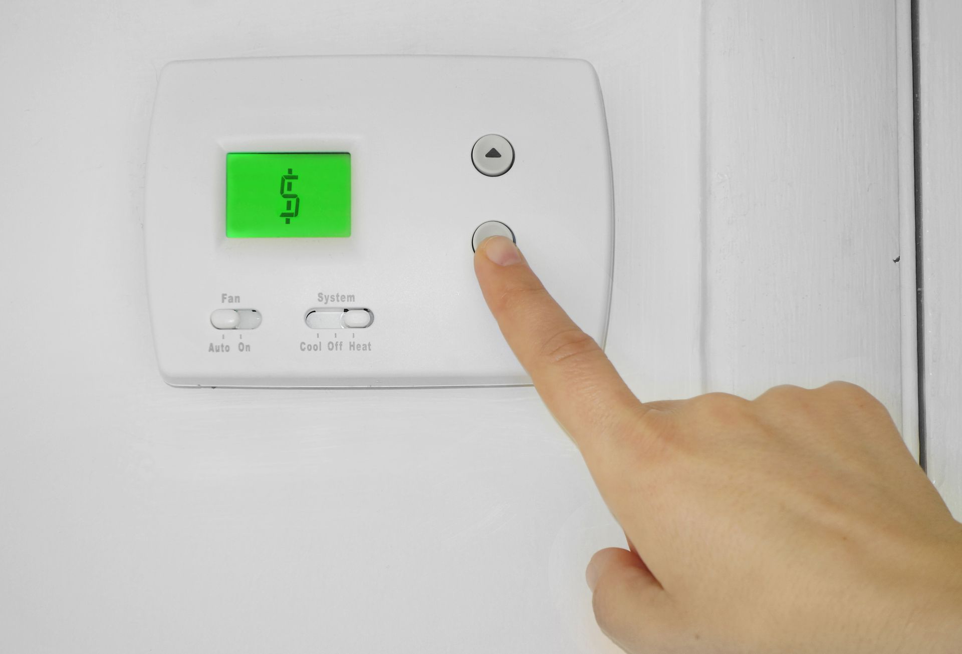 A hand punching buttons on an air conditioning control panel with a money sign on the screen.