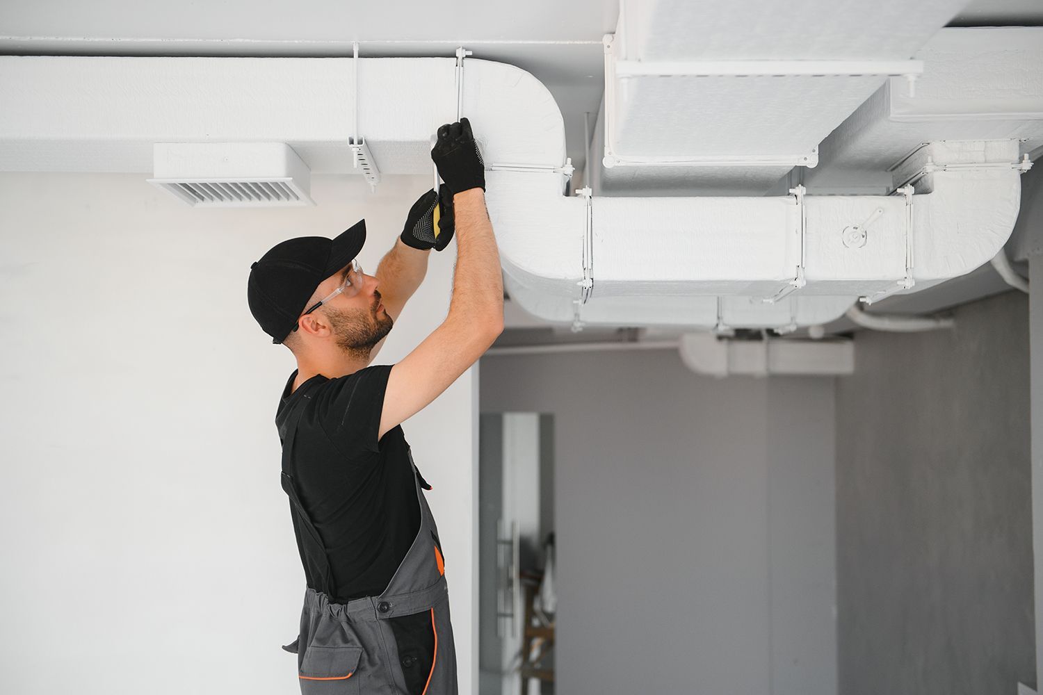 A technician wearing a black uniform is servicing a ducted air conditioning system for in a house. A technician wearing a black uniform is servicing a ducted air conditioning system for in a house.