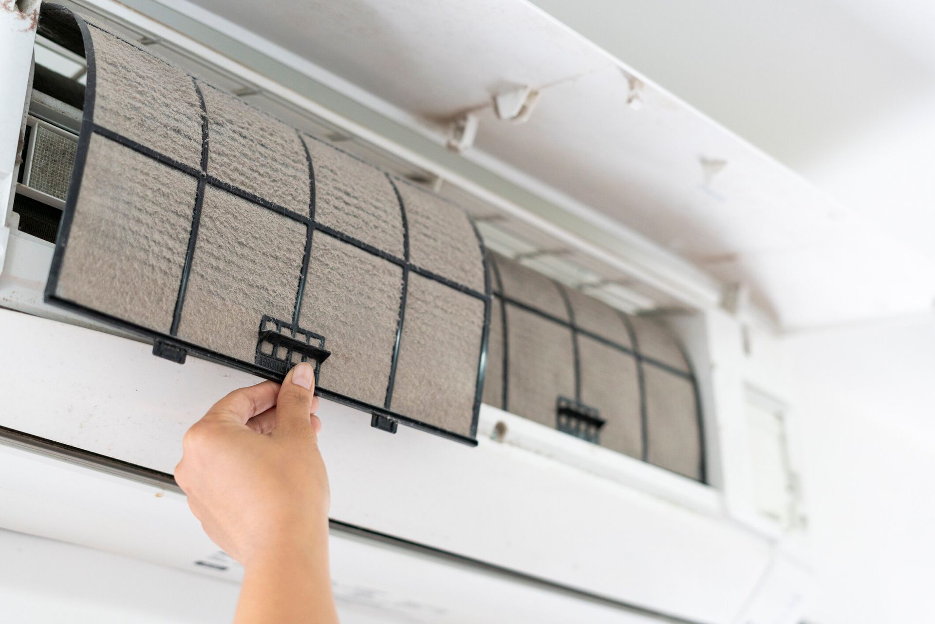 Close-up of a person taking a dirty filter from an AC unit inside a room.