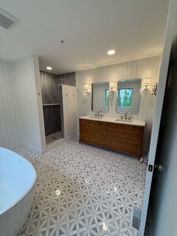 Bright modern bathroom with patterned tile floor, wood vanity, large mirror, and shower stall