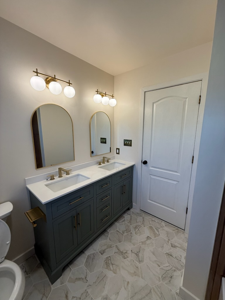 Bathroom with a blue vanity, white countertops, arched mirrors, and gold fixtures.