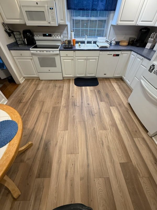 Bright kitchen with white cabinets, wood floor, black countertops, and a window over the sink.
