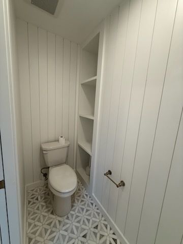 Small narrow bathroom with a toilet, patterned tile floor, and built-in shelves beside the sink.