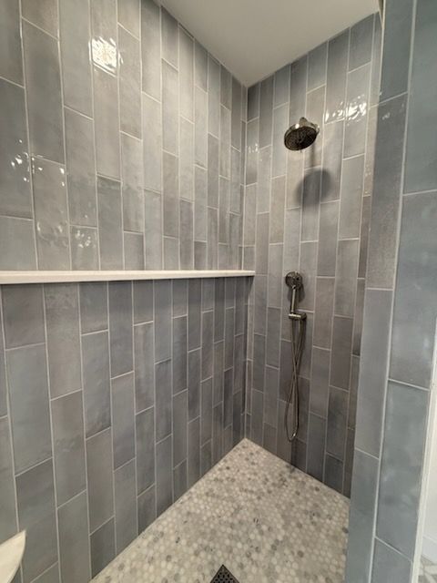 Small tiled shower stall with a built-in shelf, showerhead, and pebble-style floor.