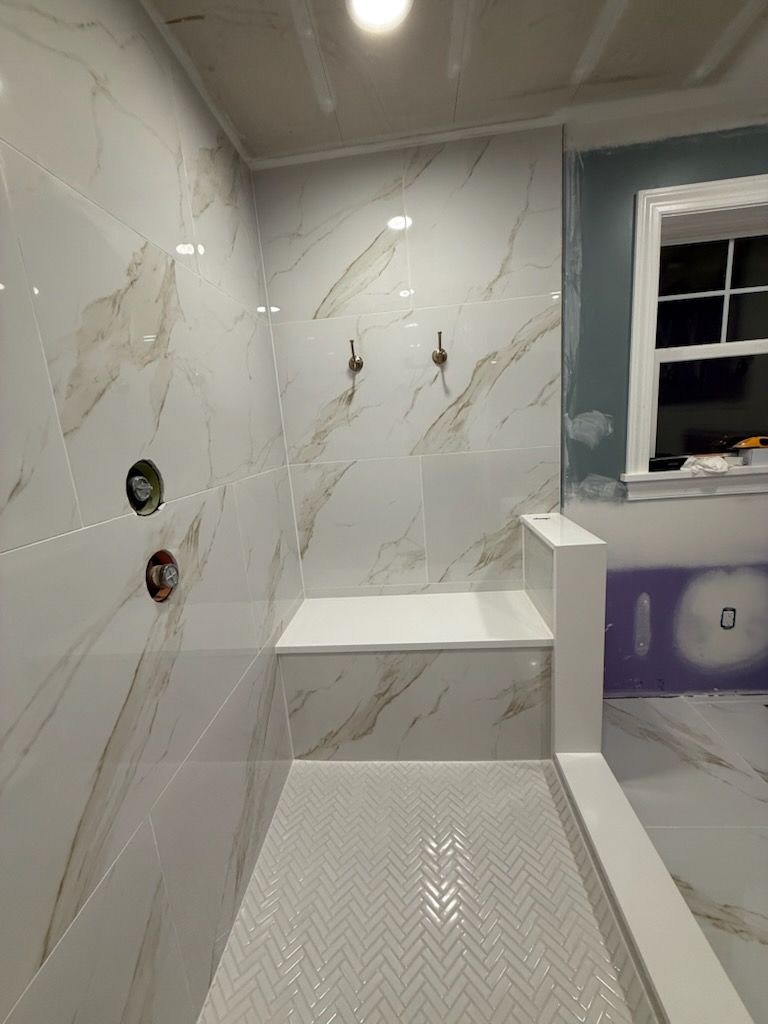 Modern tiled shower with bench, wall niches, white hex floor, and a window ledge.