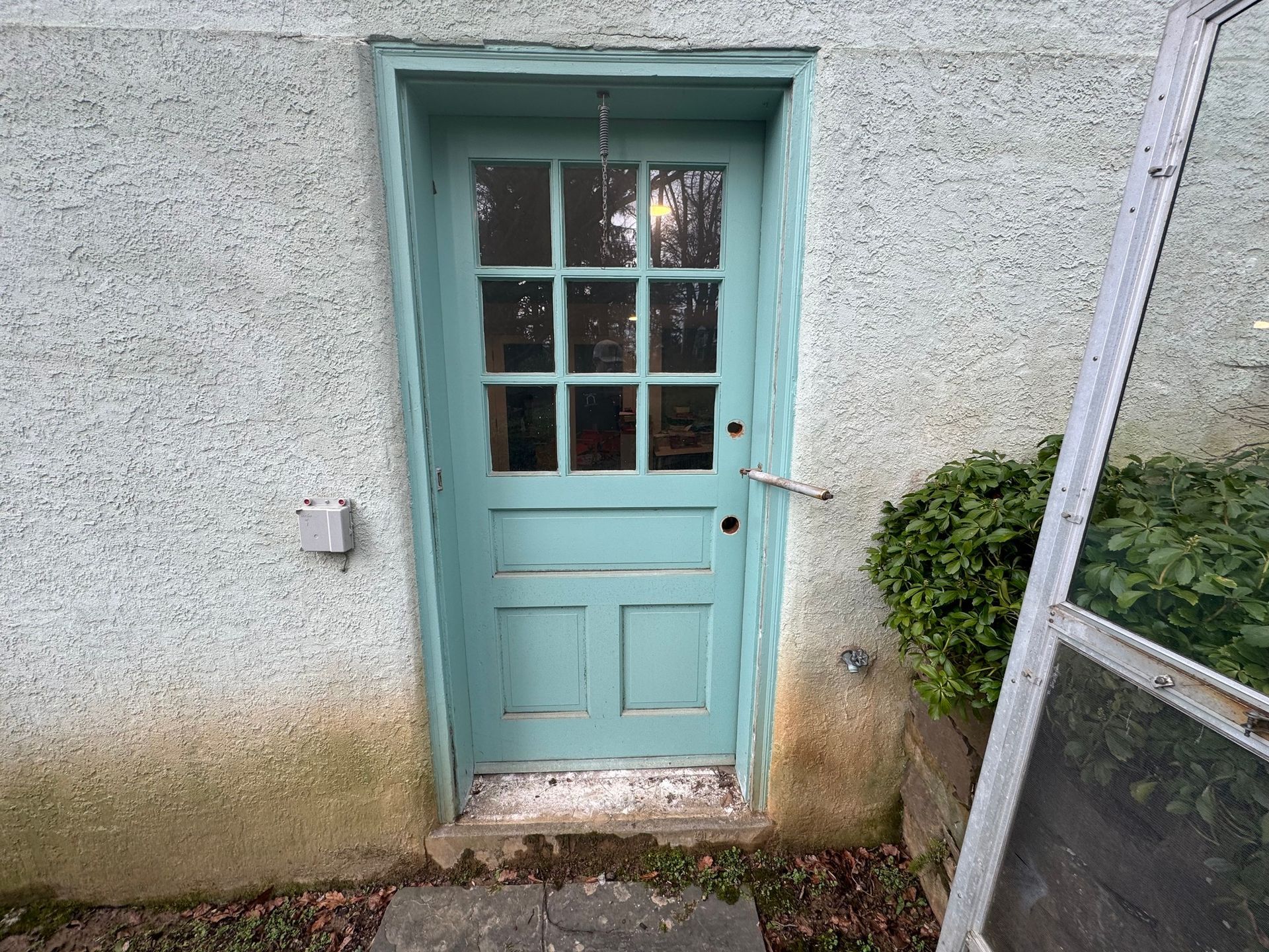 Blue door with glass panels on a stucco wall. A screen door leans beside it.
