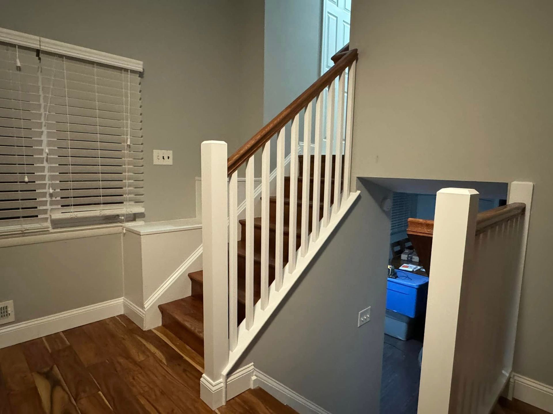 Staircase with white balusters, wood handrail and steps, leading to a doorway. Light from a window.