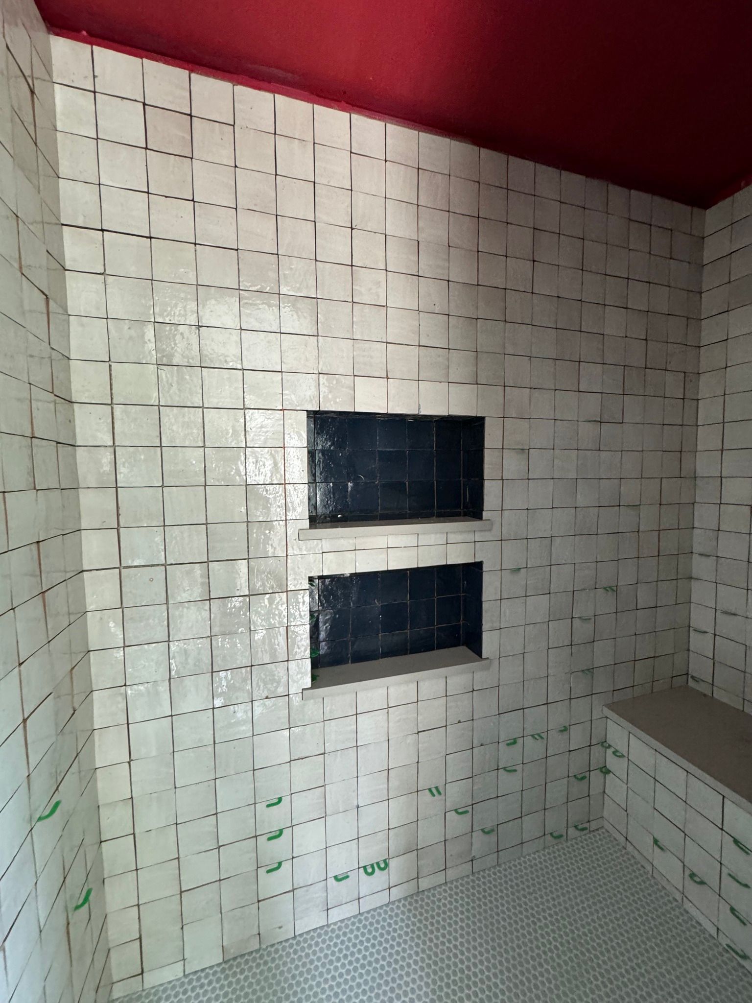 Shower with white tile walls, two built-in black niches, and a red ceiling.