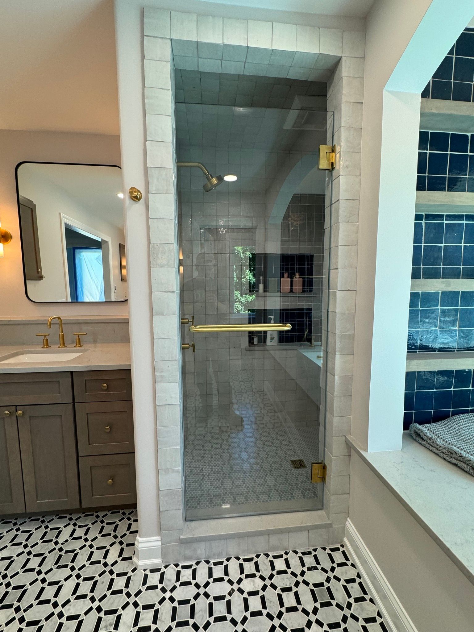 Bathroom with glass shower door, gold fixtures, patterned tile floor, and gray vanity.