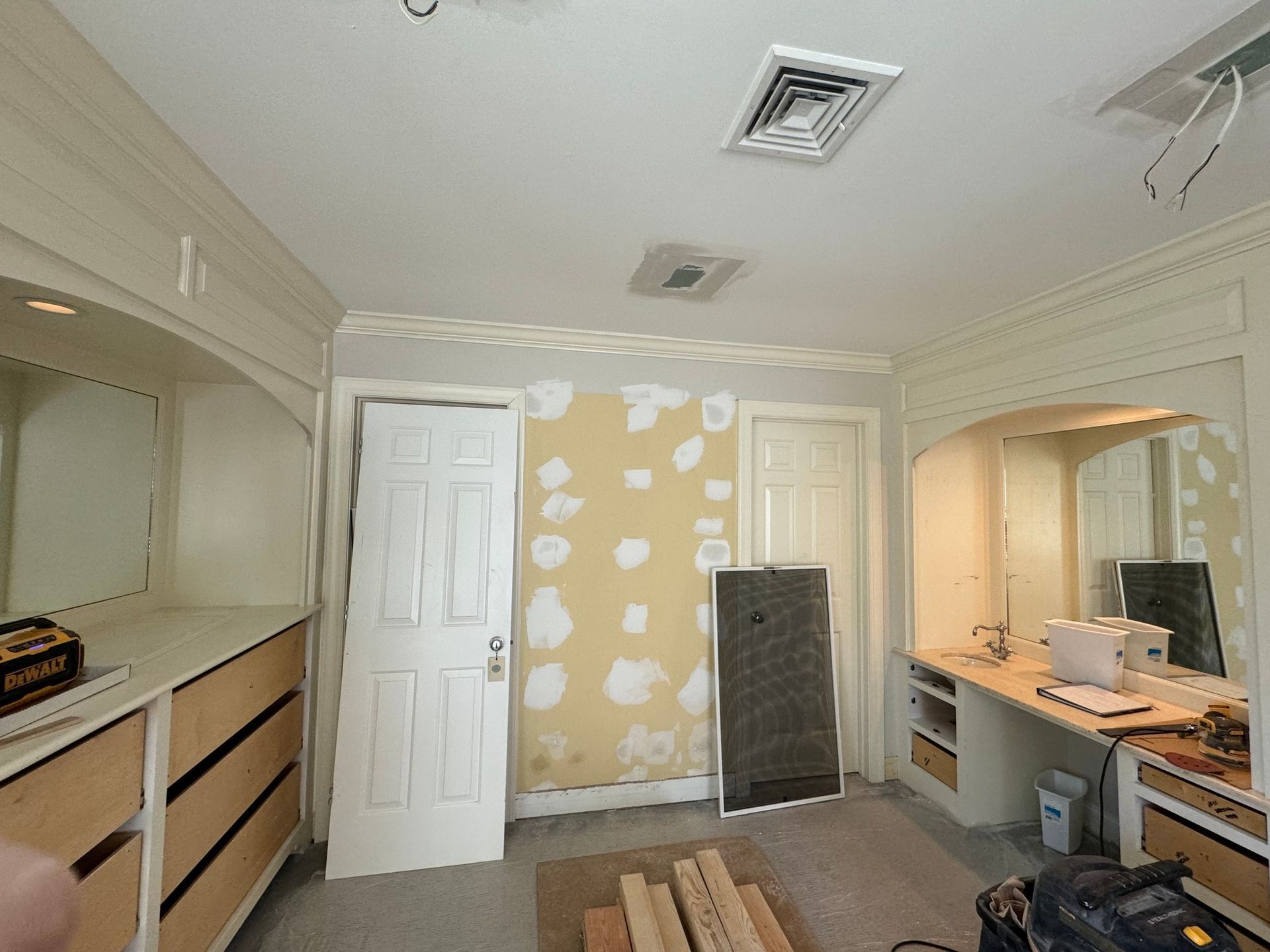 Bedroom undergoing renovation: dresser, door, and desk with mirror. Damaged walls, unfinished.