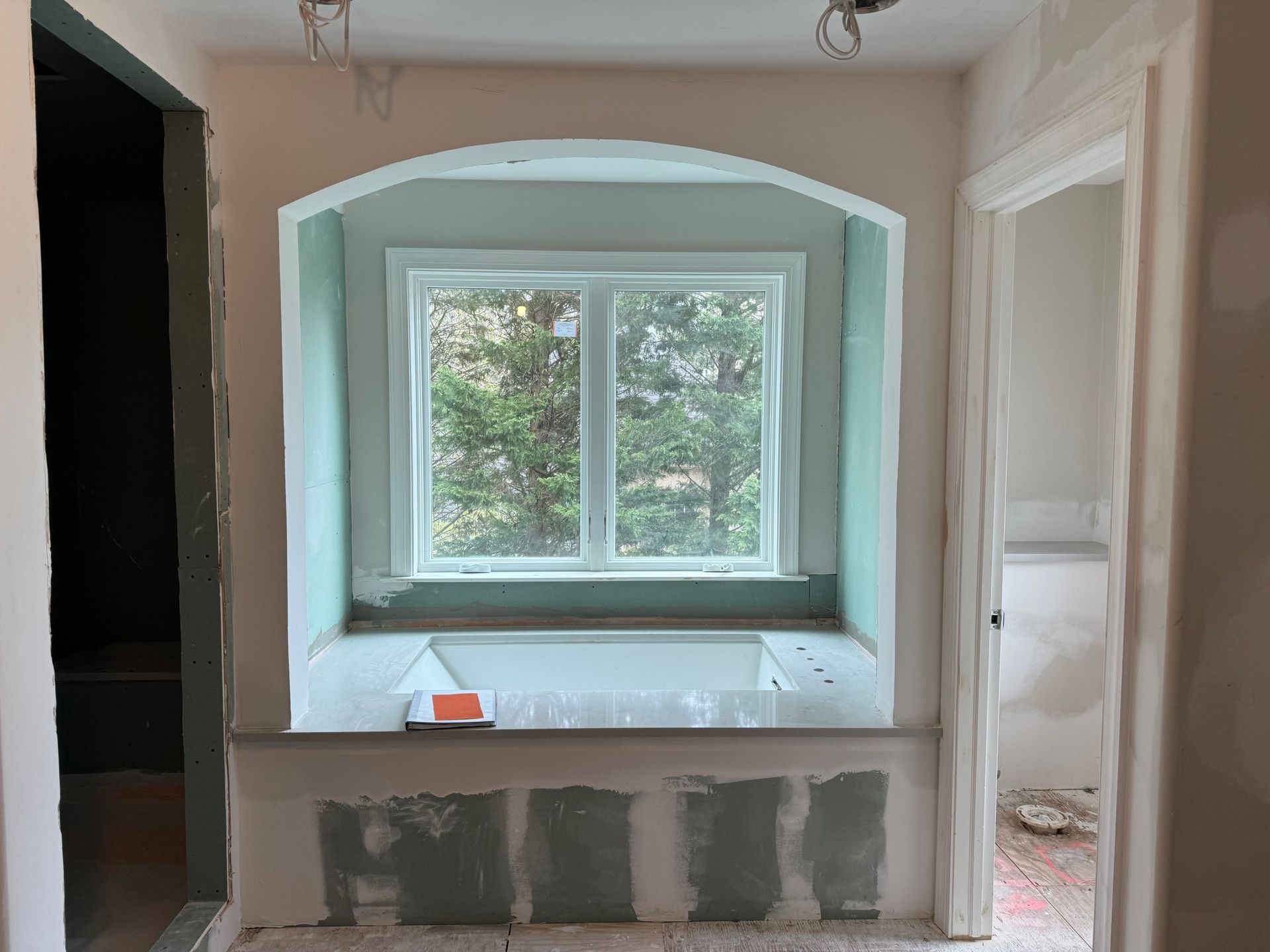 Bathroom renovation: recessed window with arched top, green walls, light wood trim, and a doorway.