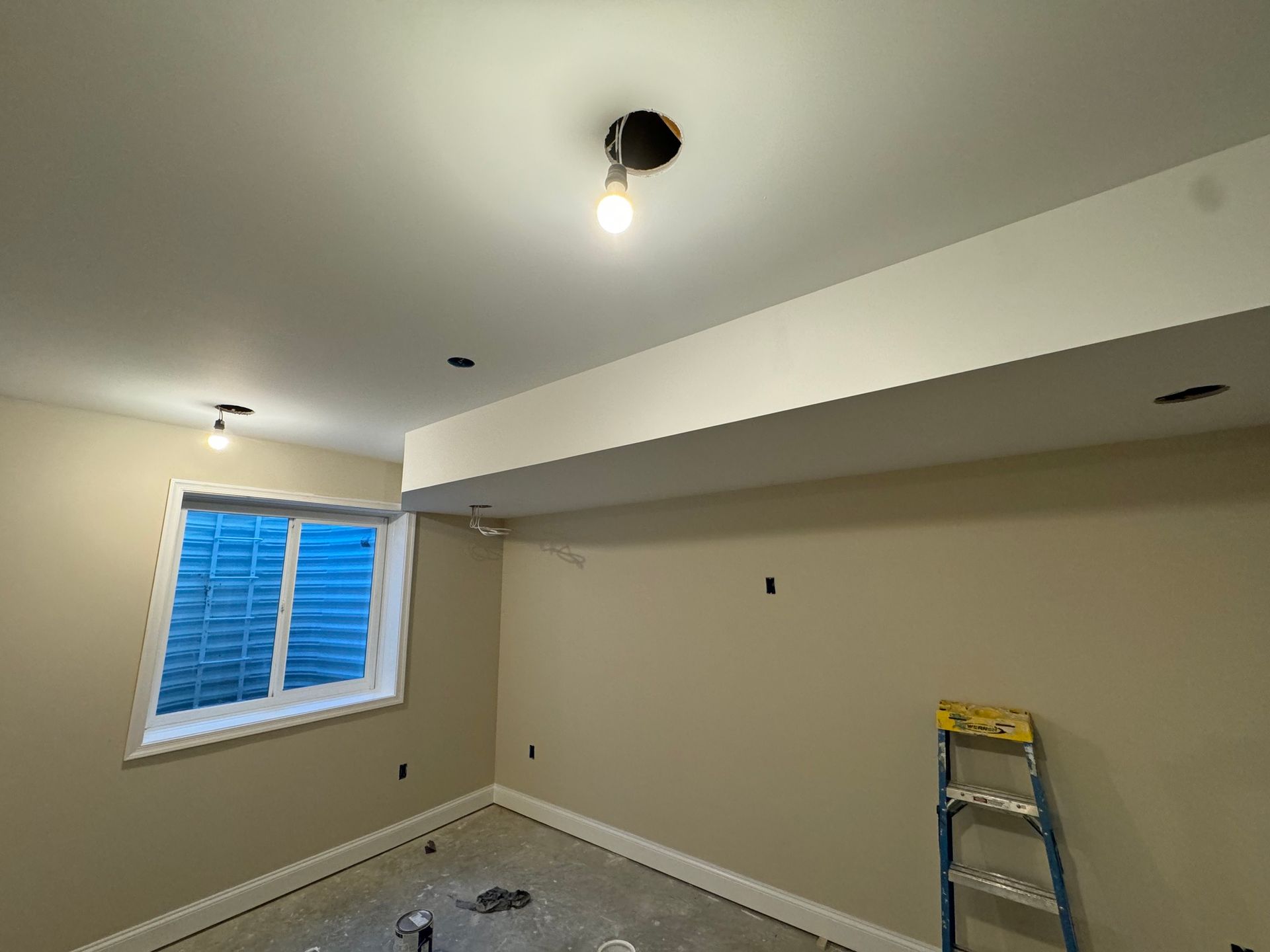 Room under construction with a window, beige walls, and exposed light fixtures.