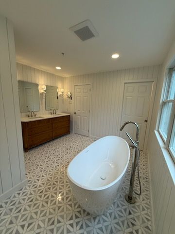Bright modern bathroom with freestanding tub, patterned tile floor, double vanity, and glass shower door
