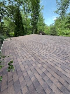 Brown shingled roof surrounded by green trees under a clear sky