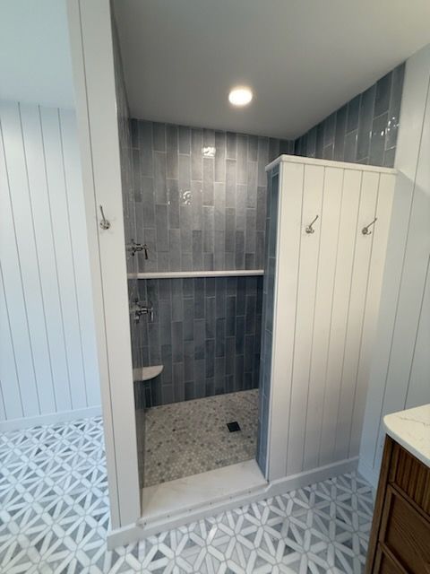 Modern bathroom with white paneled walls, gray tiled shower, and white stalls with a patterned floor.