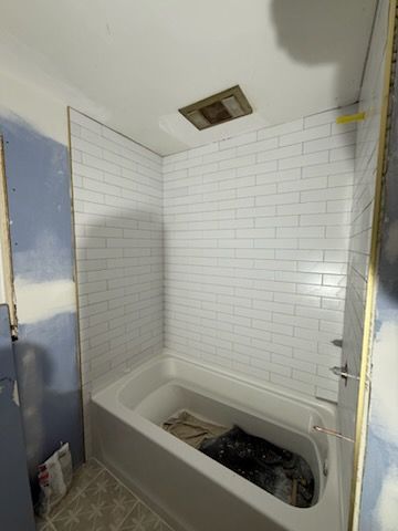 Small bathroom with a white tiled shower-tub and a ceiling light; bathtub contains tools or debris.