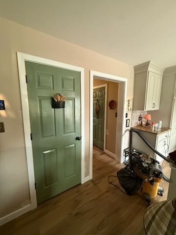 Interior entryway with green front door, beige walls, wood floor, and cleaning supplies near a console table