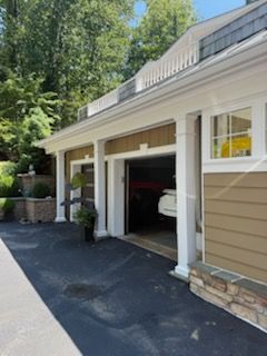 Row of beige garage bays with white trim beside a driveway and trees