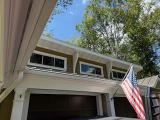 Two-story house garage with an American flag hanging beside the door under a blue sky.