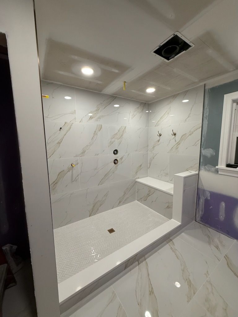 Modern white bathroom with marble-look tile, walk-in shower, recessed lights, and a sink vanity