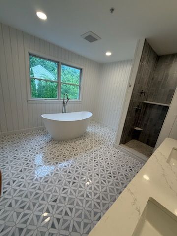 Bright modern bathroom with freestanding tub, patterned tile floor, and window by the sink.