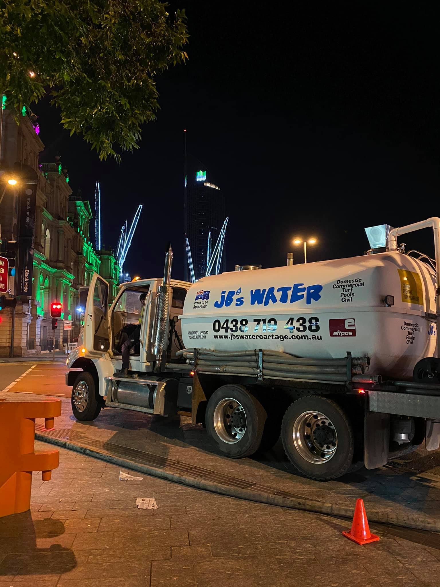 Street-cleaning truck parked at night beside orange cones on a lit city street