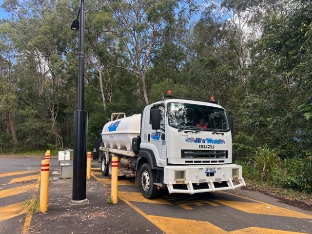 White utility truck parked beside yellow bollards at a wooded roadside checkpoint.