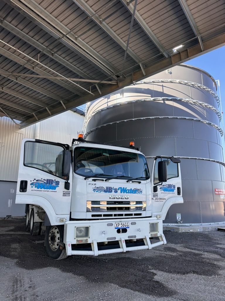 White truck parked under a metal canopy beside a large industrial tank