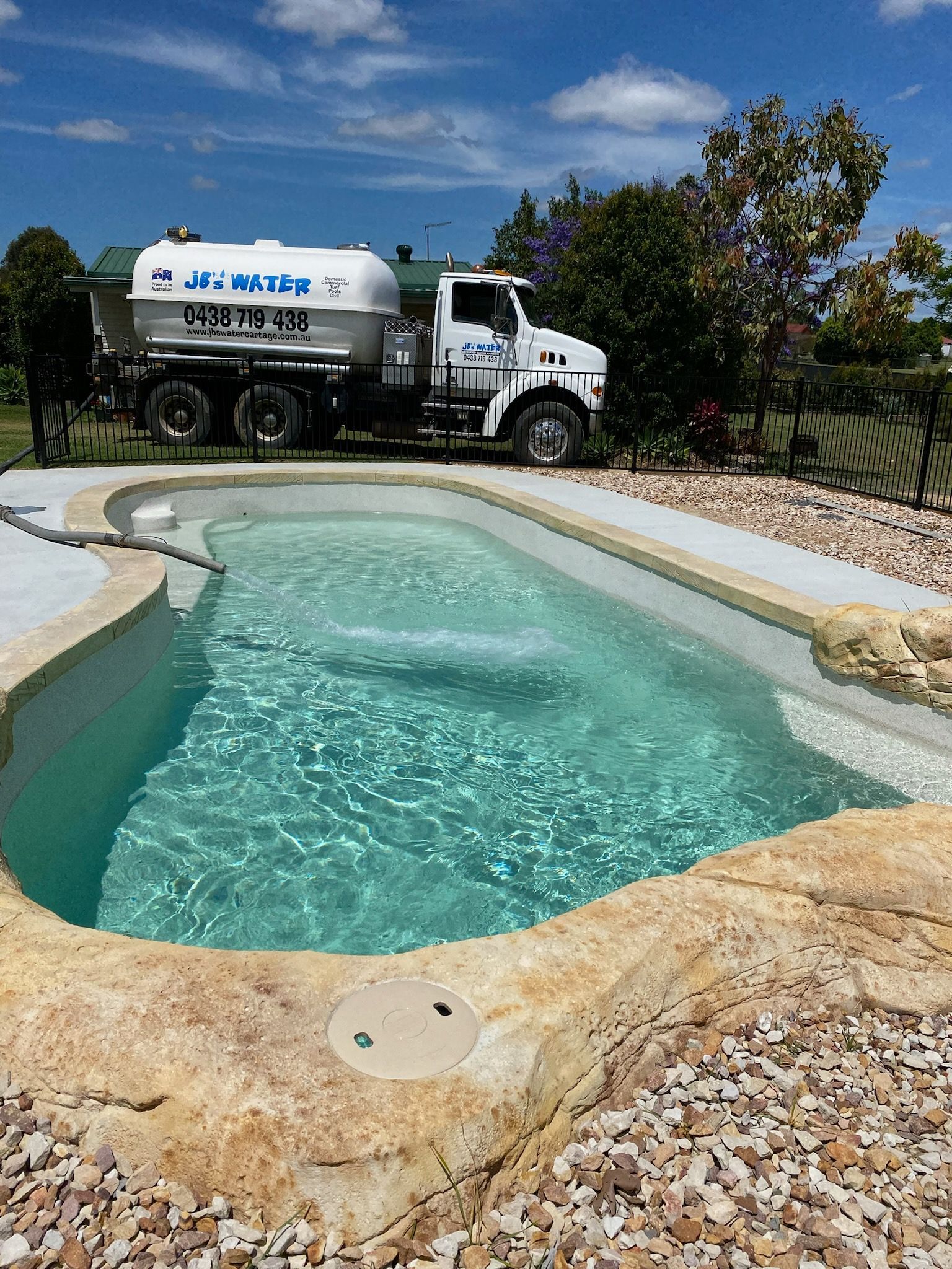 Concrete swimming pool with turquoise water and a water tanker truck in the background under a blue sky