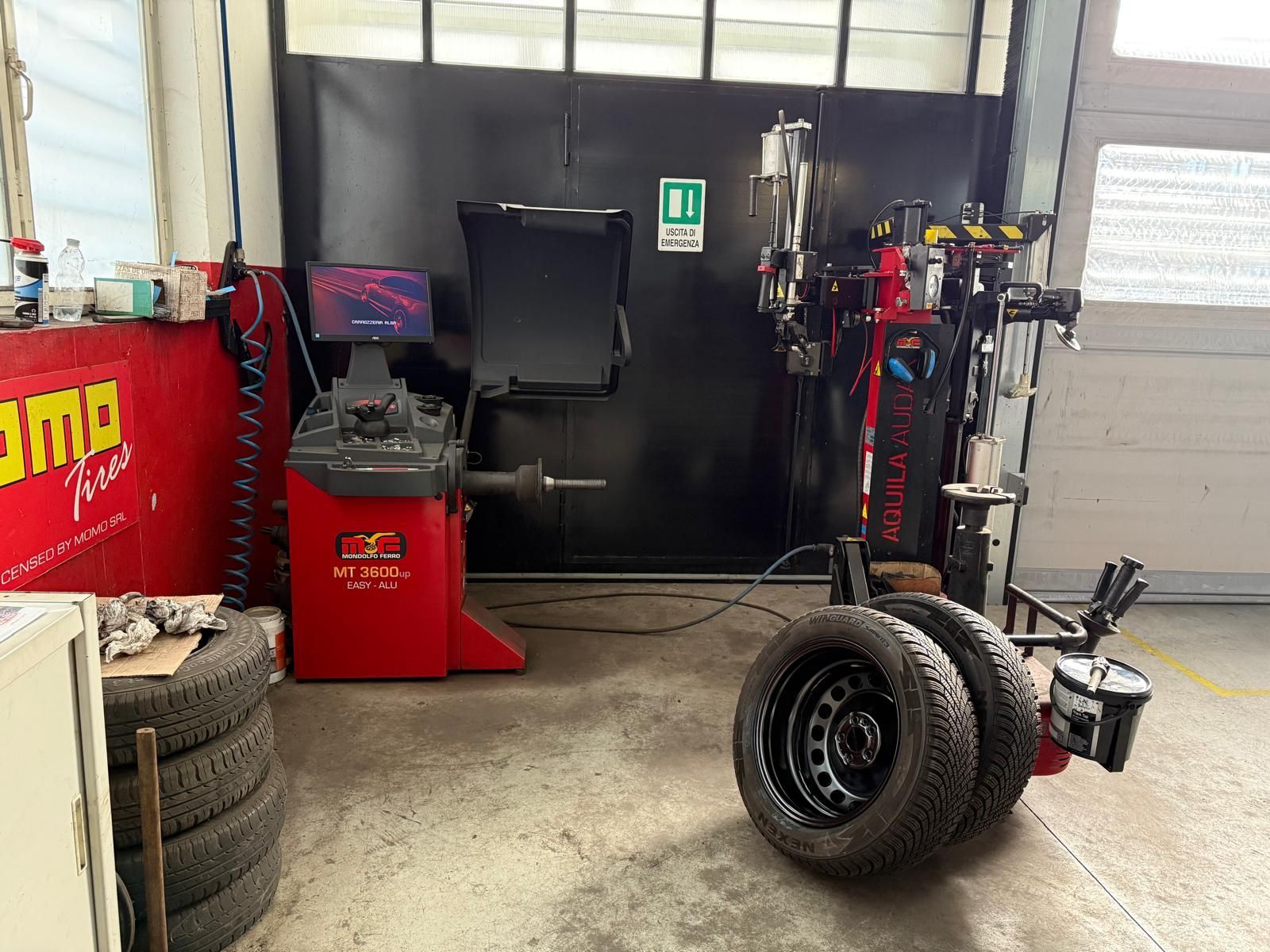 Una macchina equilibratrice per pneumatici si trova in un garage accanto a una pila di pneumatici.