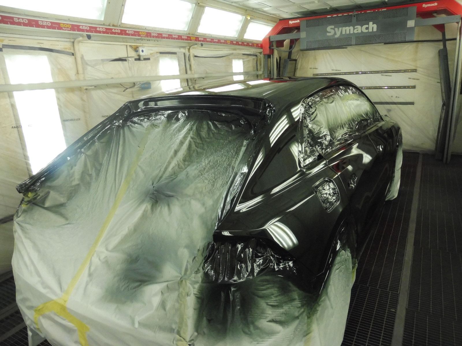 Un'auto nera viene verniciata in una cabina di verniciatura Symach