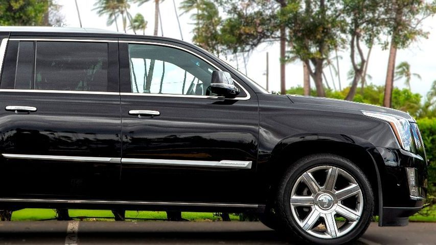 Black Cadillac SUV parked outdoors with trees in background.