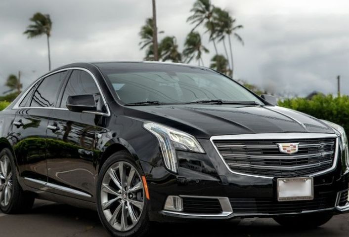 Black Cadillac sedan parked outdoors under a cloudy sky with palm trees.