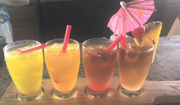 Four colorful tropical drinks in glasses with straws, one with a parasol and a pineapple slice.