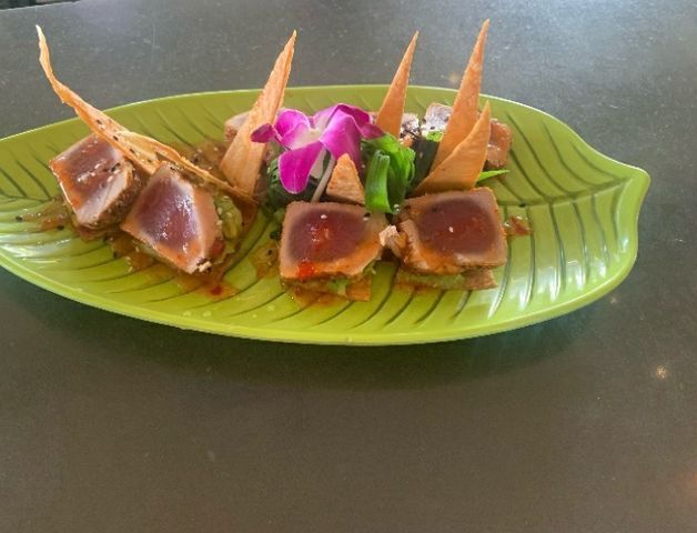 Seared tuna dish on a green leaf-shaped plate, garnished with chips and an orchid.
