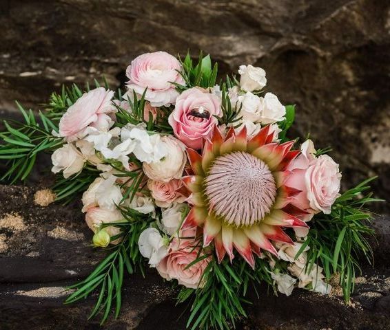 Wedding bouquet with pink roses, protea, and greenery on a textured stone.