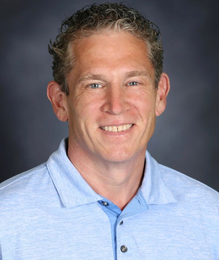 Headshot of a smiling man in a light blue polo shirt against a gray background