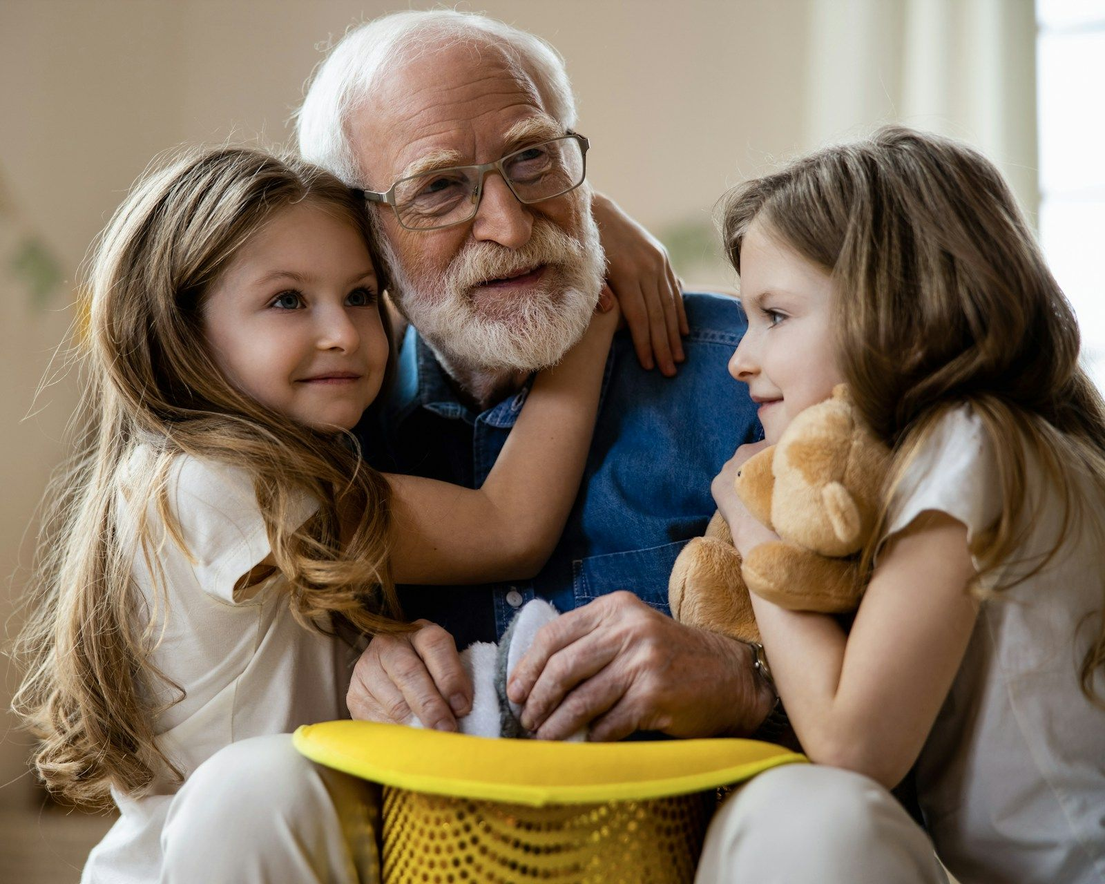 Three people cuddling on a couch, with an older man holding a yellow basket and smiling between two children.