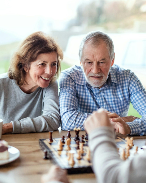 Two people smiling over a chess game at a table in a bright room