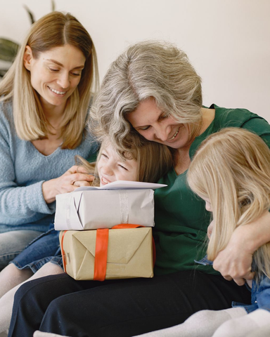 Three people opening wrapped gifts on a couch, smiling together indoors