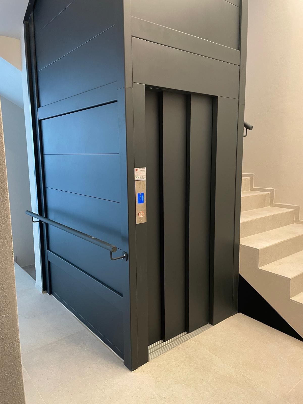 Ascensore nero accanto a una scala in un corridoio interno moderno