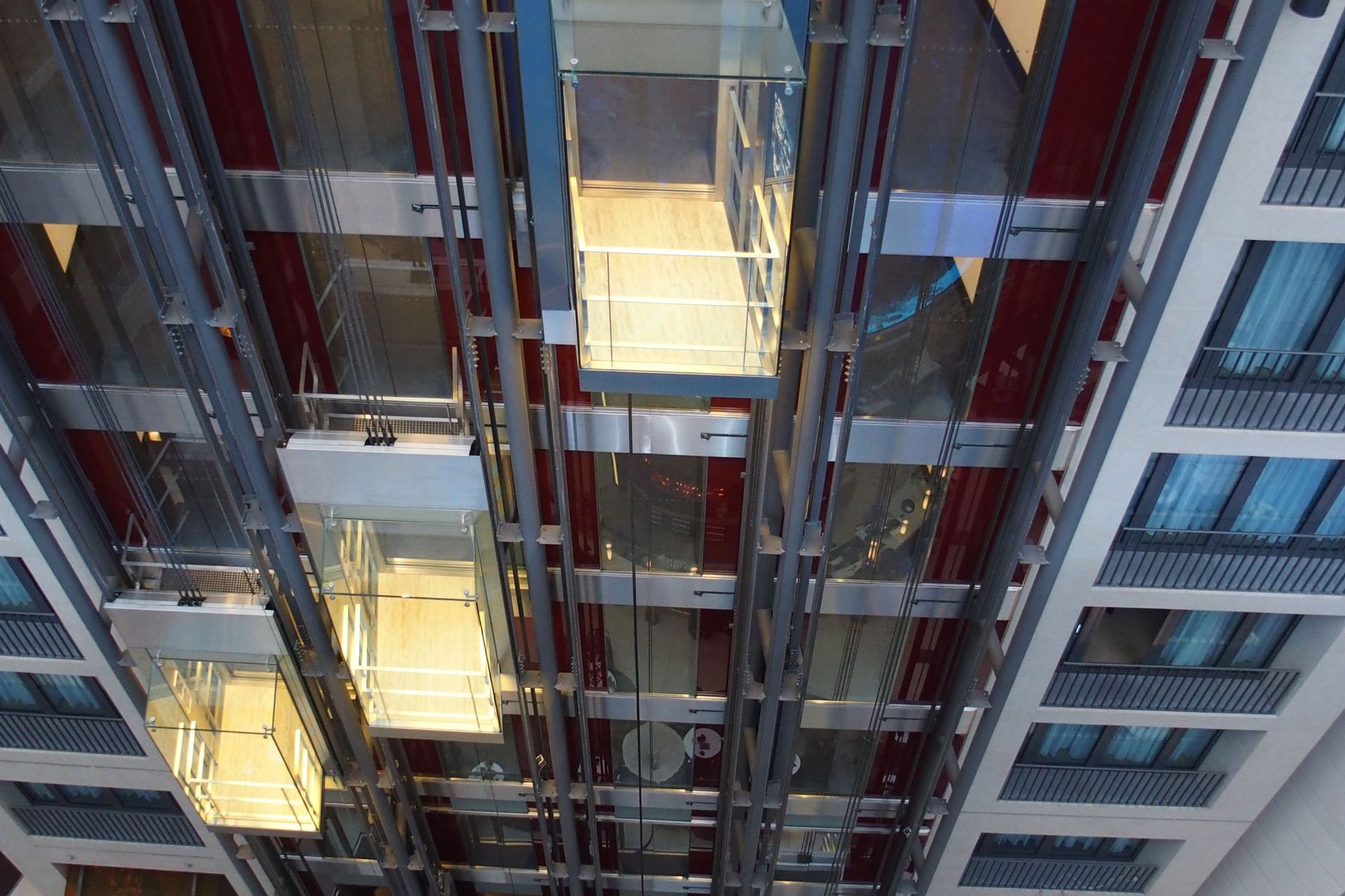 Ascensori in un edificio alto, visti dal basso. Le cabine in vetro salgono e scendono in vani aperti.