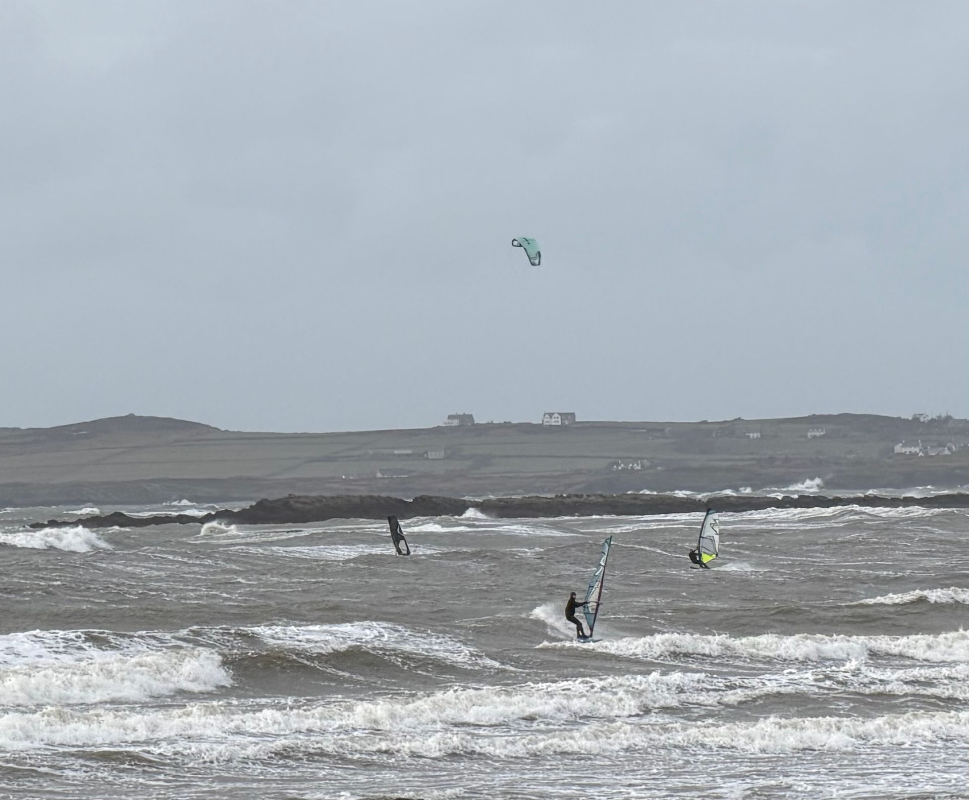 Windy gray seascape with choppy waves and three kite surfers in the distance.