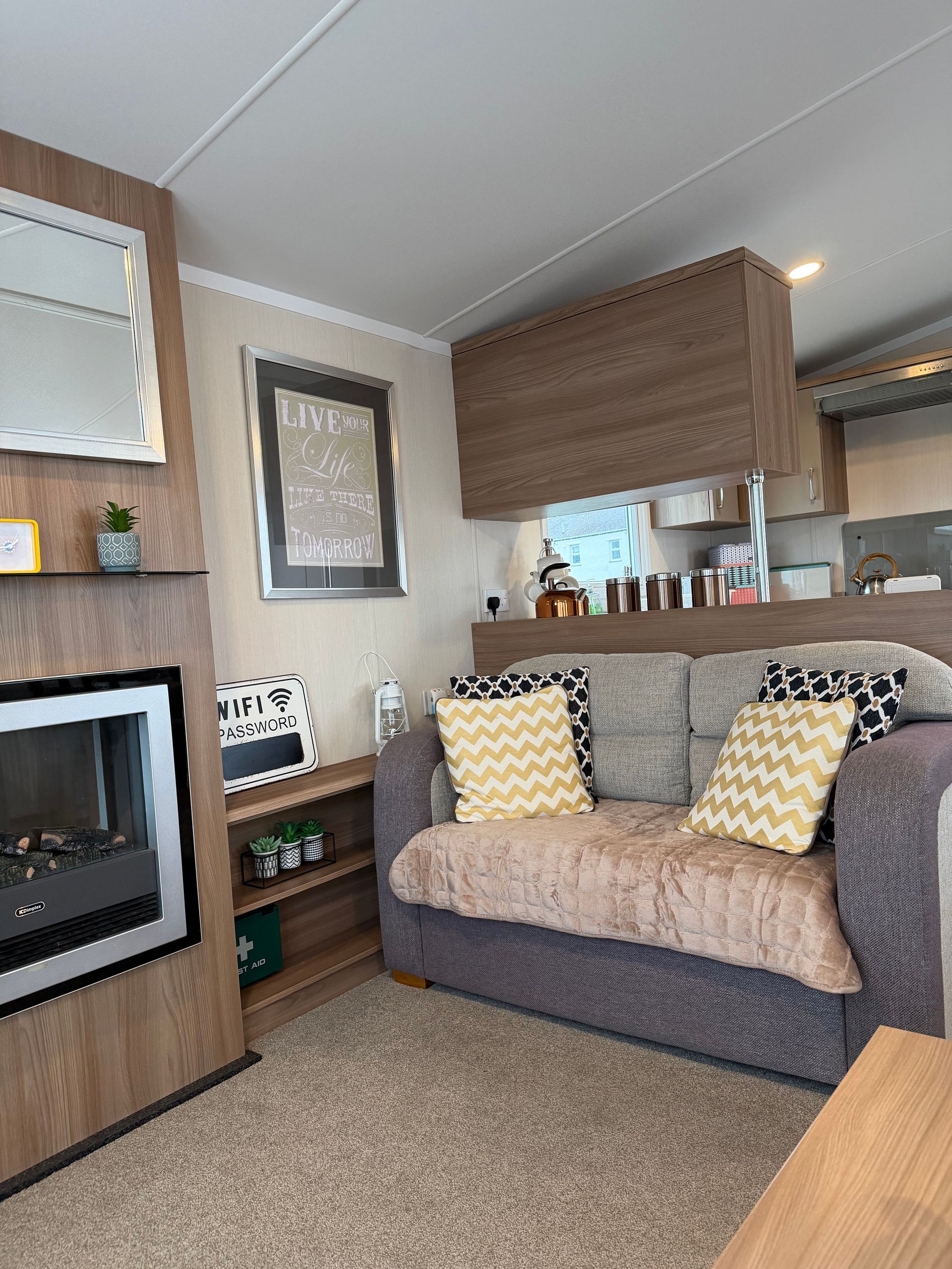Cozy living room with a fireplace, gray sofa with yellow pillows, and a kitchen pass-through in the background