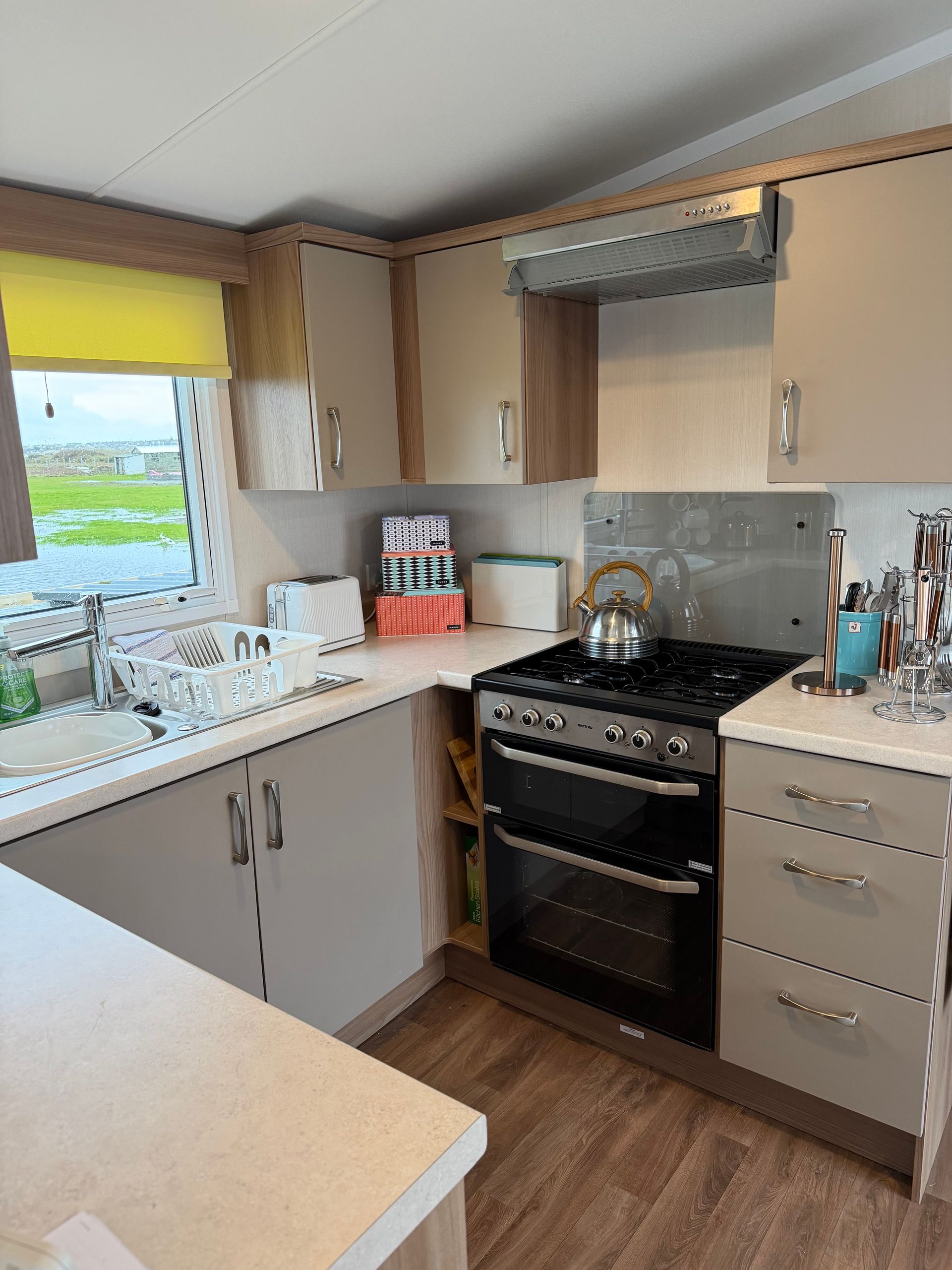 Small kitchen with gray cabinets, black stove, beige countertops, and a window above the sink