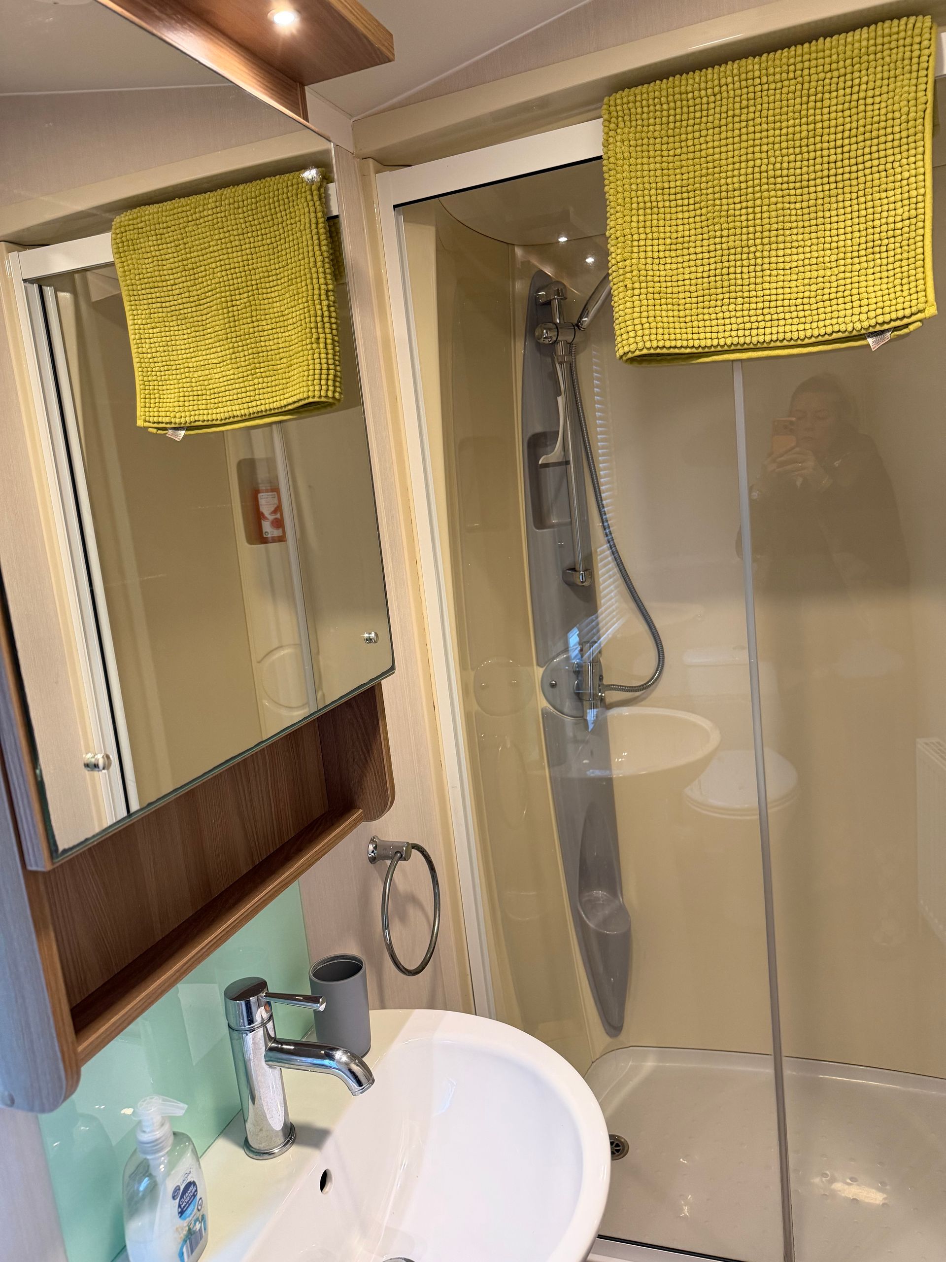 Small bathroom with white sink, mirror, glass shower, and yellow towels.