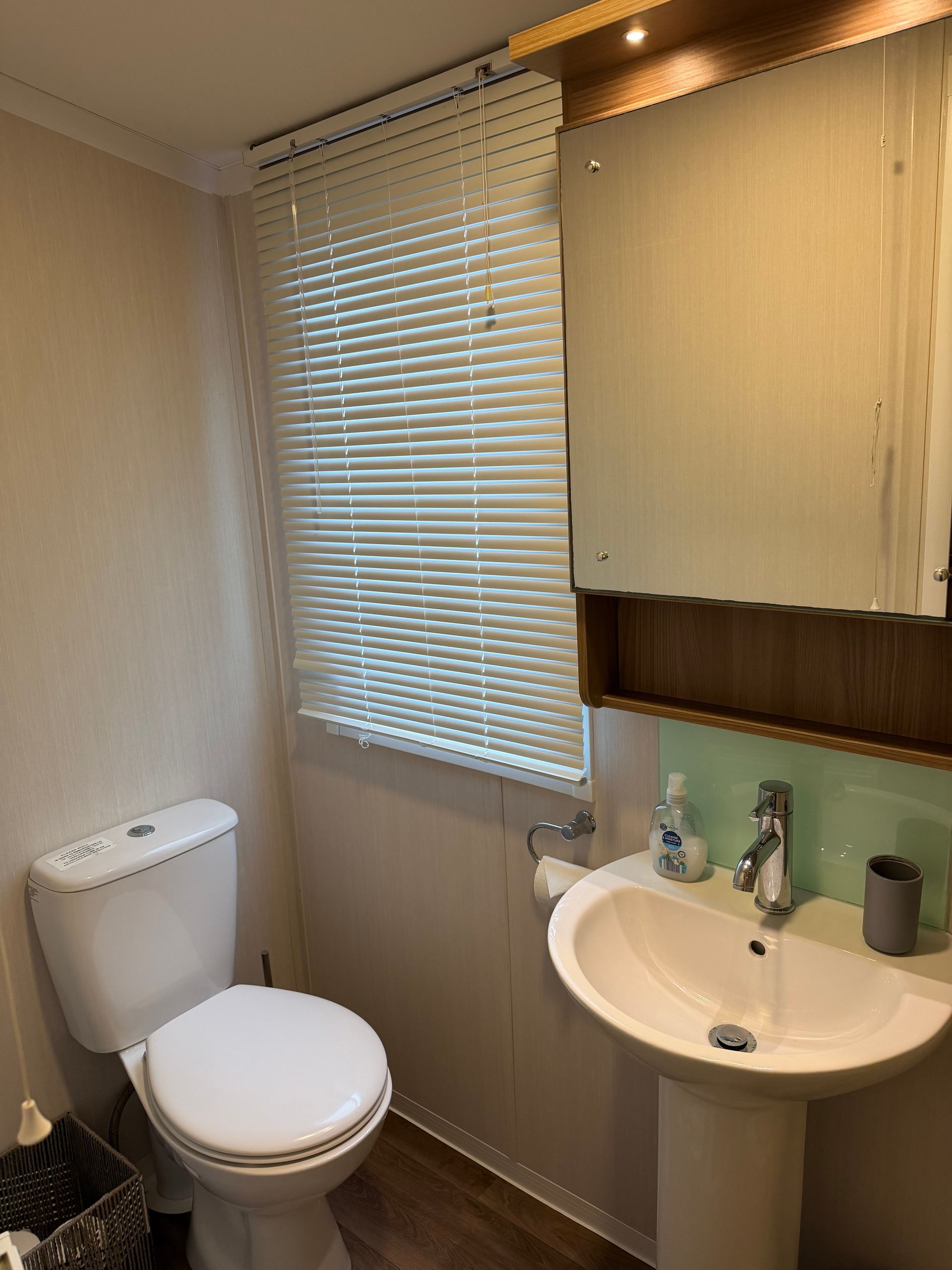 Small bathroom with toilet, sink, mirror cabinet, and window with blinds