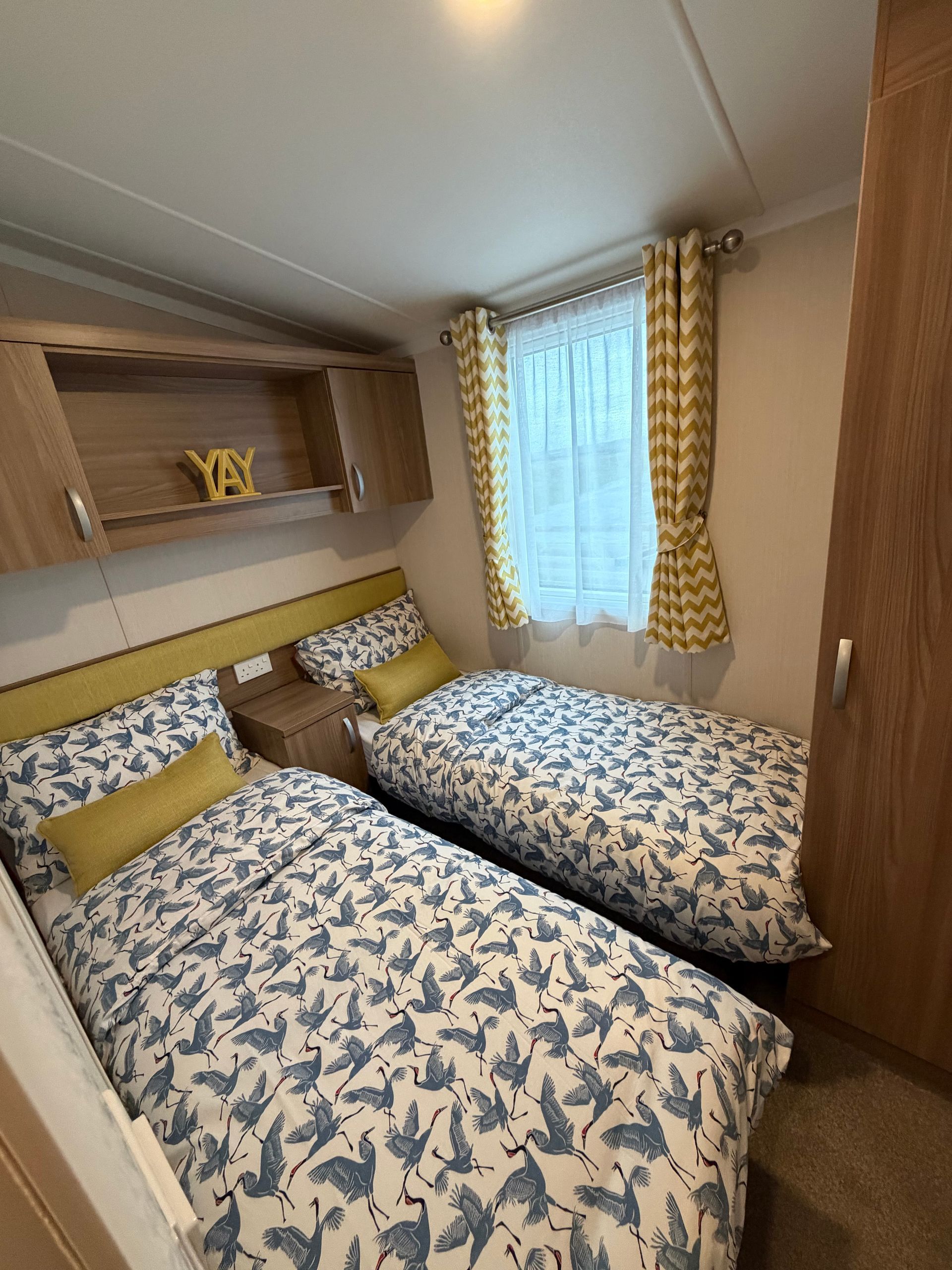 Small bedroom with two twin beds, blue floral bedding, and yellow curtains beside a window.